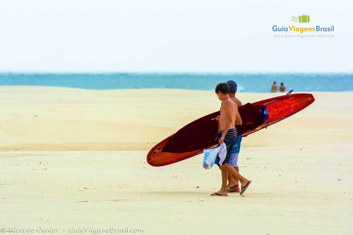 Imagem de surfistas andando nas areias da linda praia.
