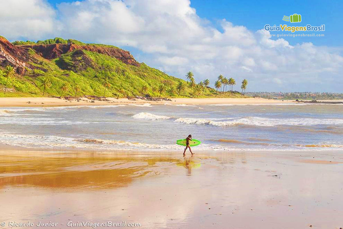 Imagem de um surfista andando com sua prancha na beira do mar.