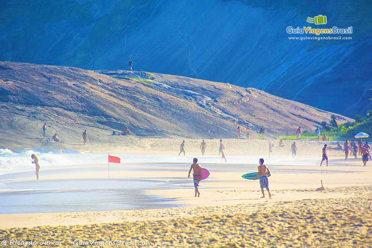 Imagem de surfistas andando com suas pranchas na areia da Praia Itacoatiara.