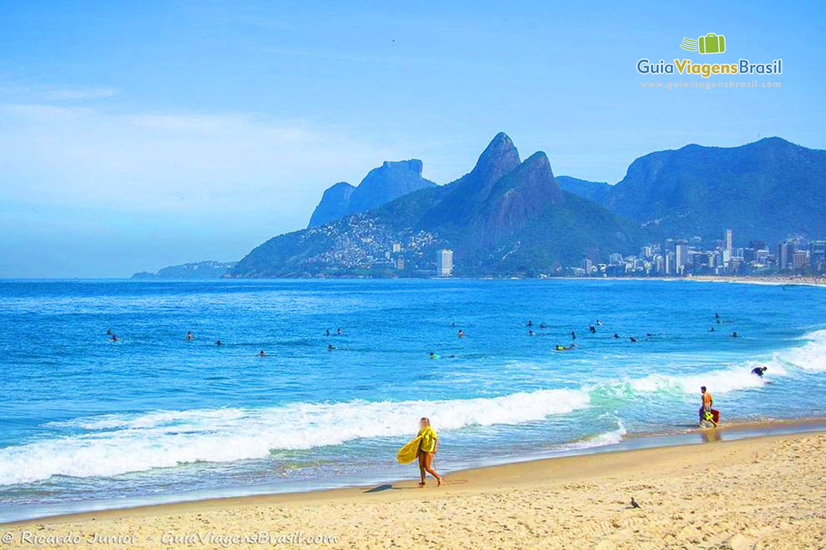 Imagem de uma menina com sua prancha vendo seus colegas no mar.