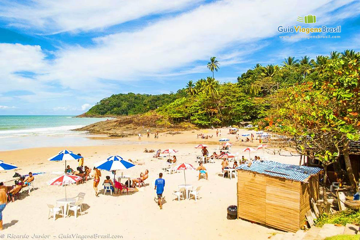 Imagem de um simples quiosque e turistas nas areias da Praia Tiririca.