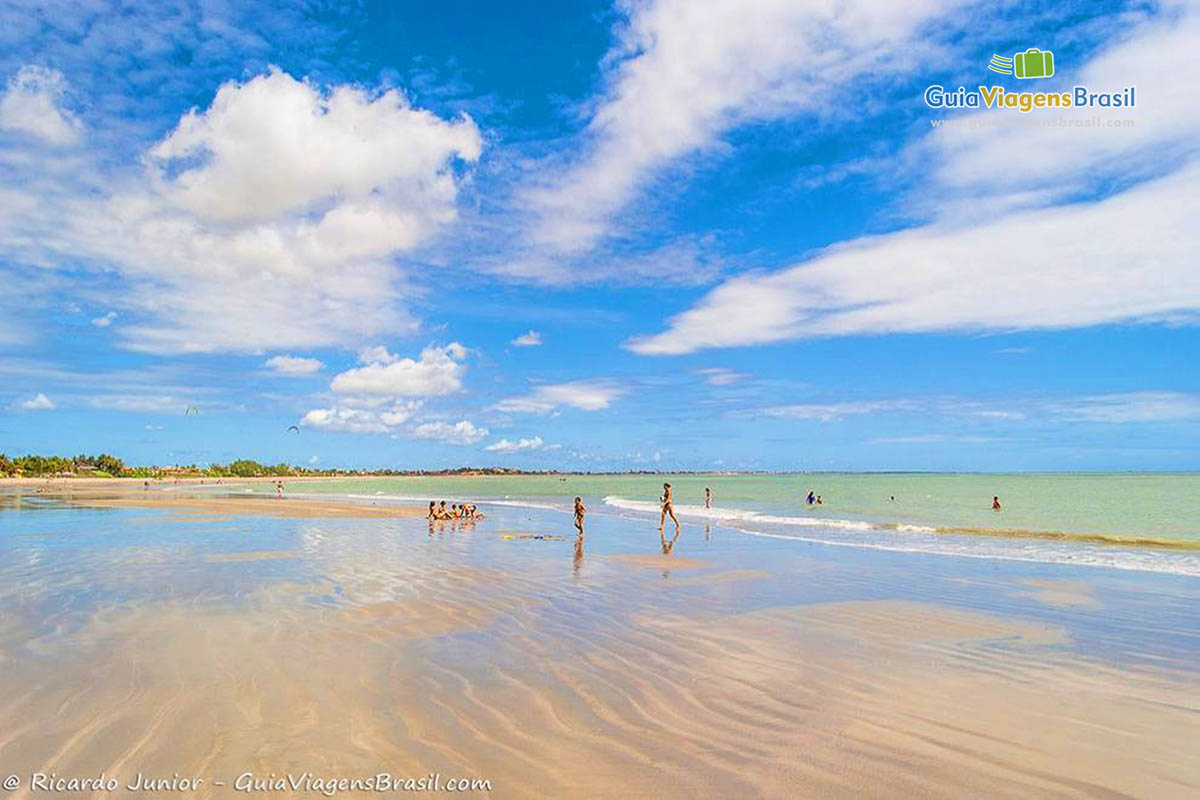 Imagem de crianças e adultos aproveitando uma bela tarde de sol na praia.