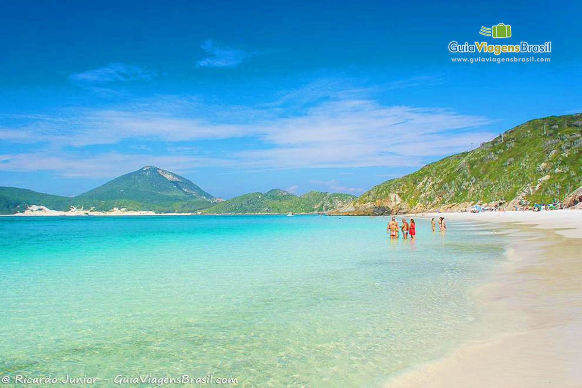 Imagem de turistas em pé no beira da praia batendo papo.