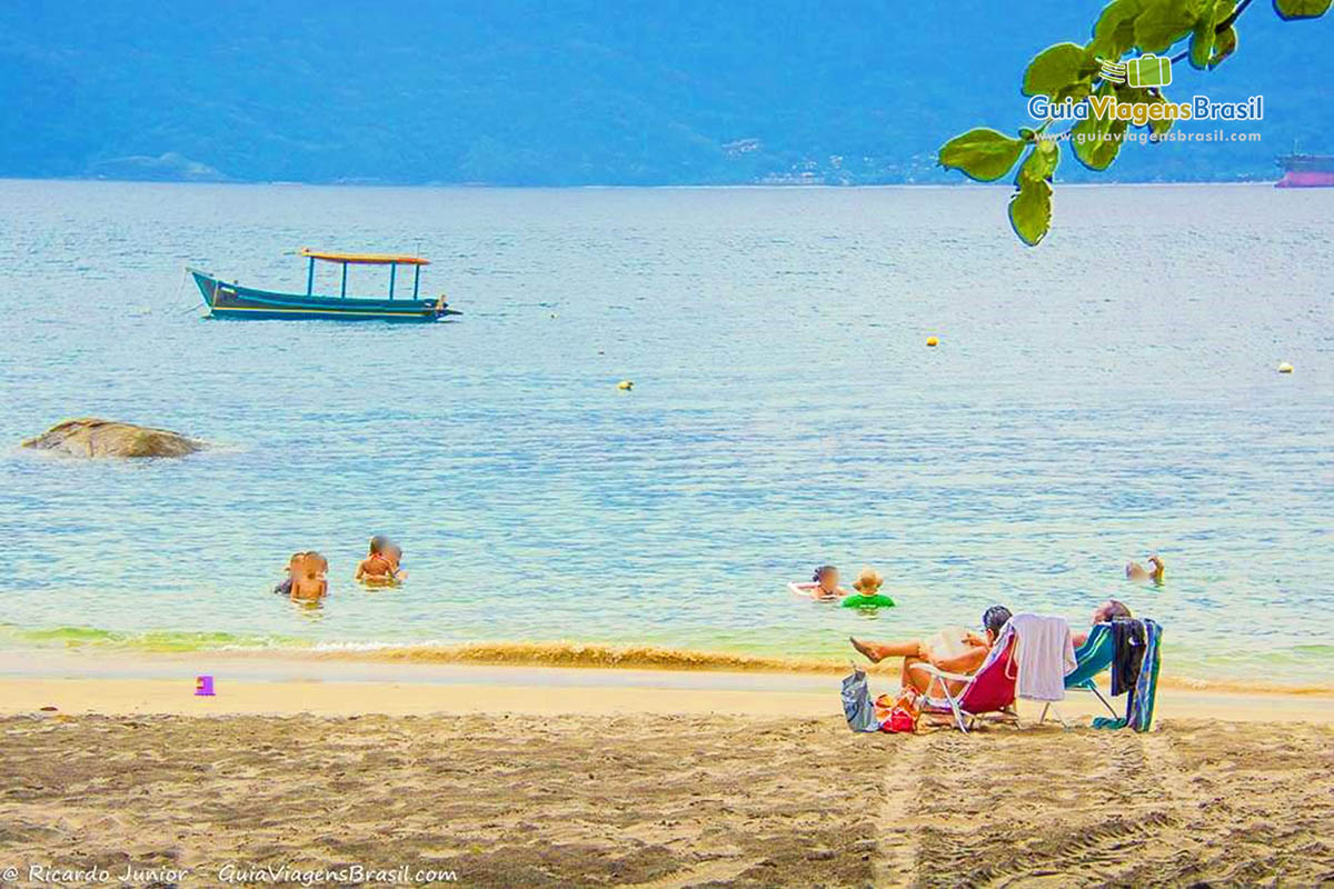 Imagem da bela Praia do Veloso com pessoas na areia e no mar curtindo um lindo dia.