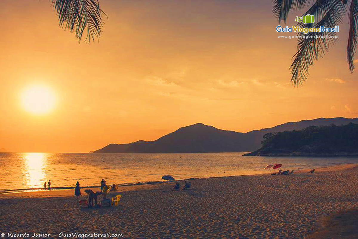 Imagem de turistas na Praia que possui bela paisagem do por do sol.