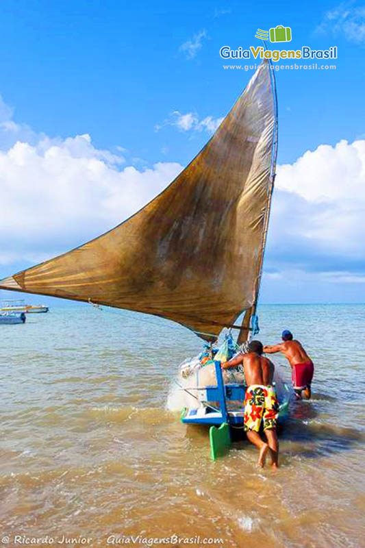 Imagem de rapazes empurrando barco para o mar.