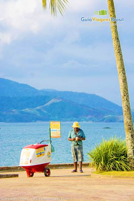 Imagem de um carrinho de sorvete com vendedor e ao fundo a linda Praia Grande.