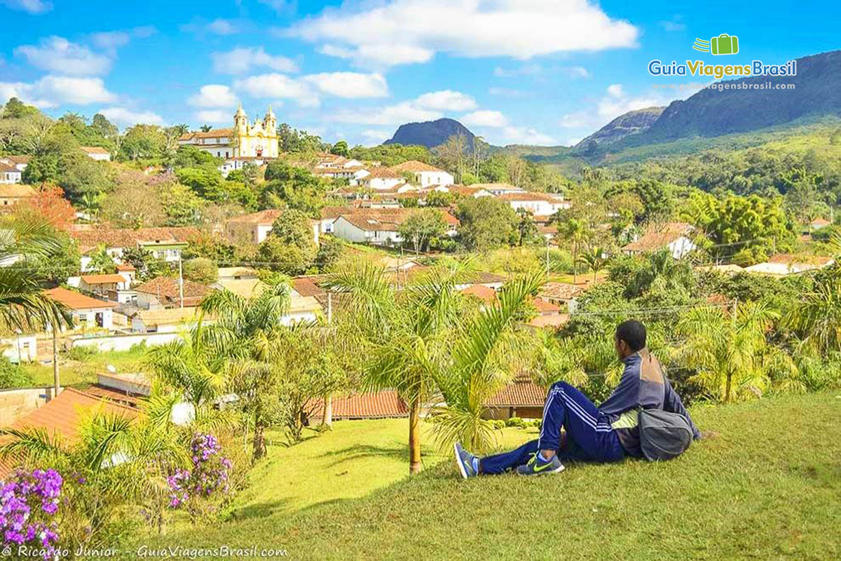Imagem de um turistas sentados em um gramado admirando a cidade do alto.