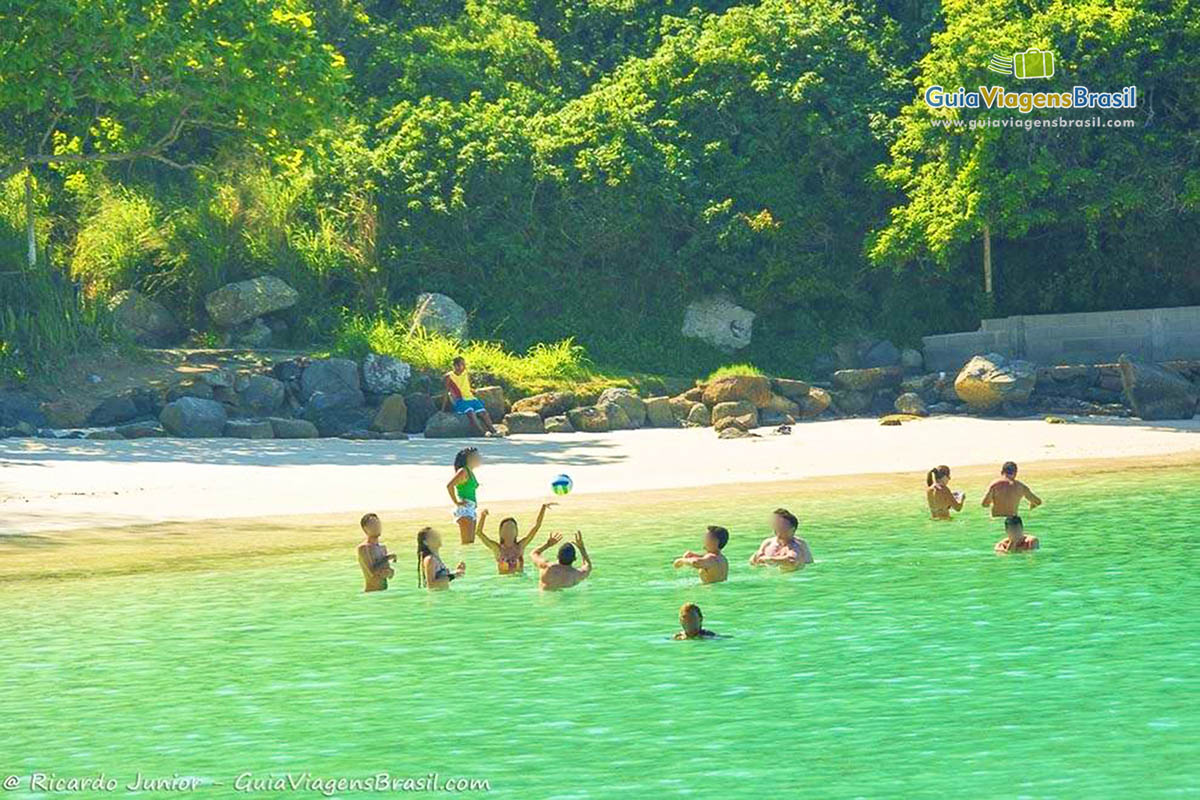 Imagem de pessoas dentro o mar jogando vôlei.